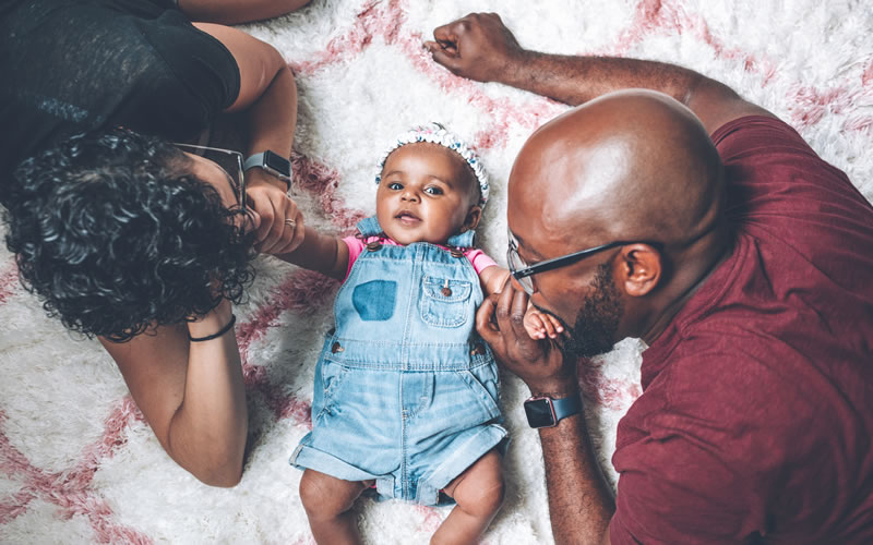 A beautiful smiling baby surrounded by her parents